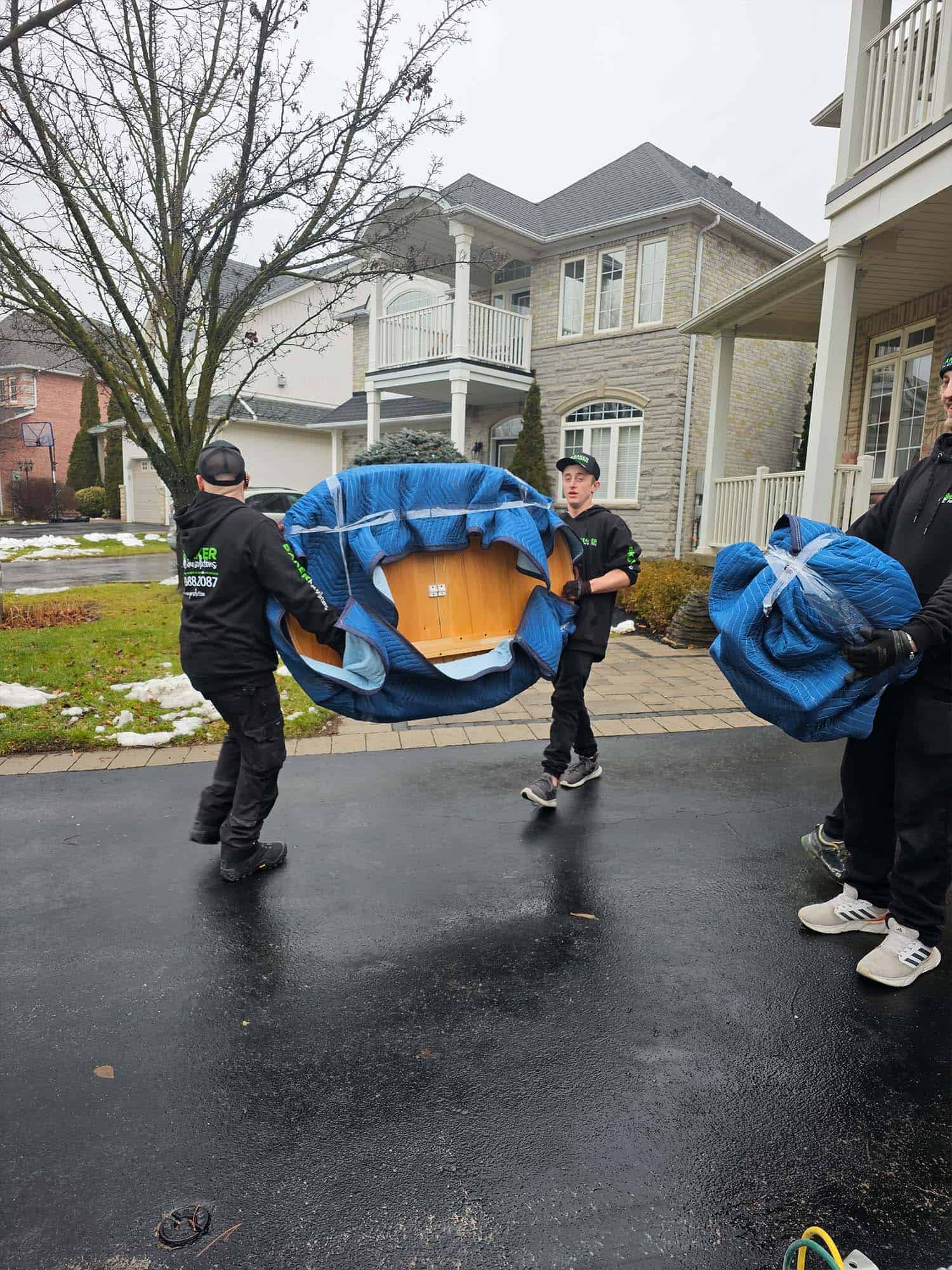 Heavy-duty movers carrying a large piece of furniture in front of a modern house.