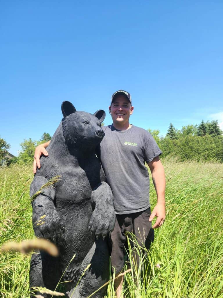 Outdoor scene with a bear sculpture and a smiling man in work uniform outdoors.