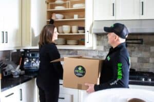 Alt text: Baker Home Solutions delivery person handing over boxes to a woman in a modern kitchen.