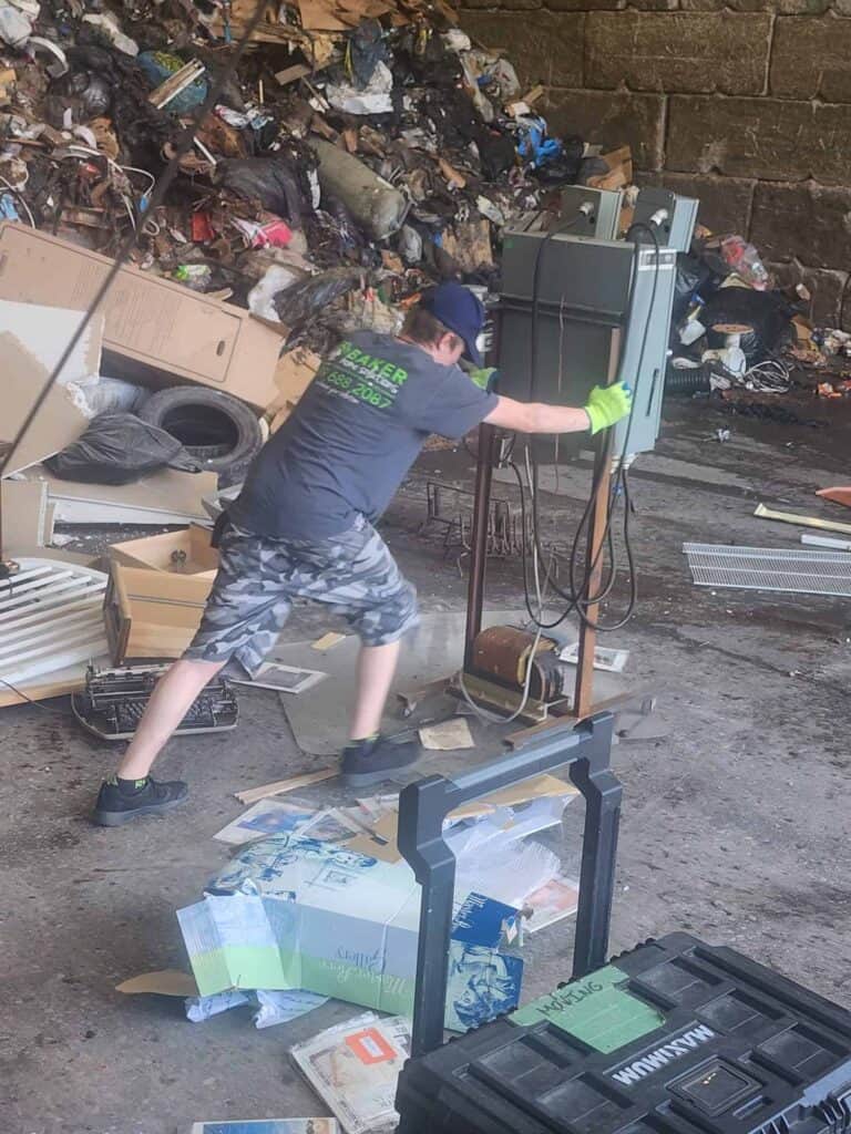 Young man repairing electrical panel amidst outdoor trash and debris.