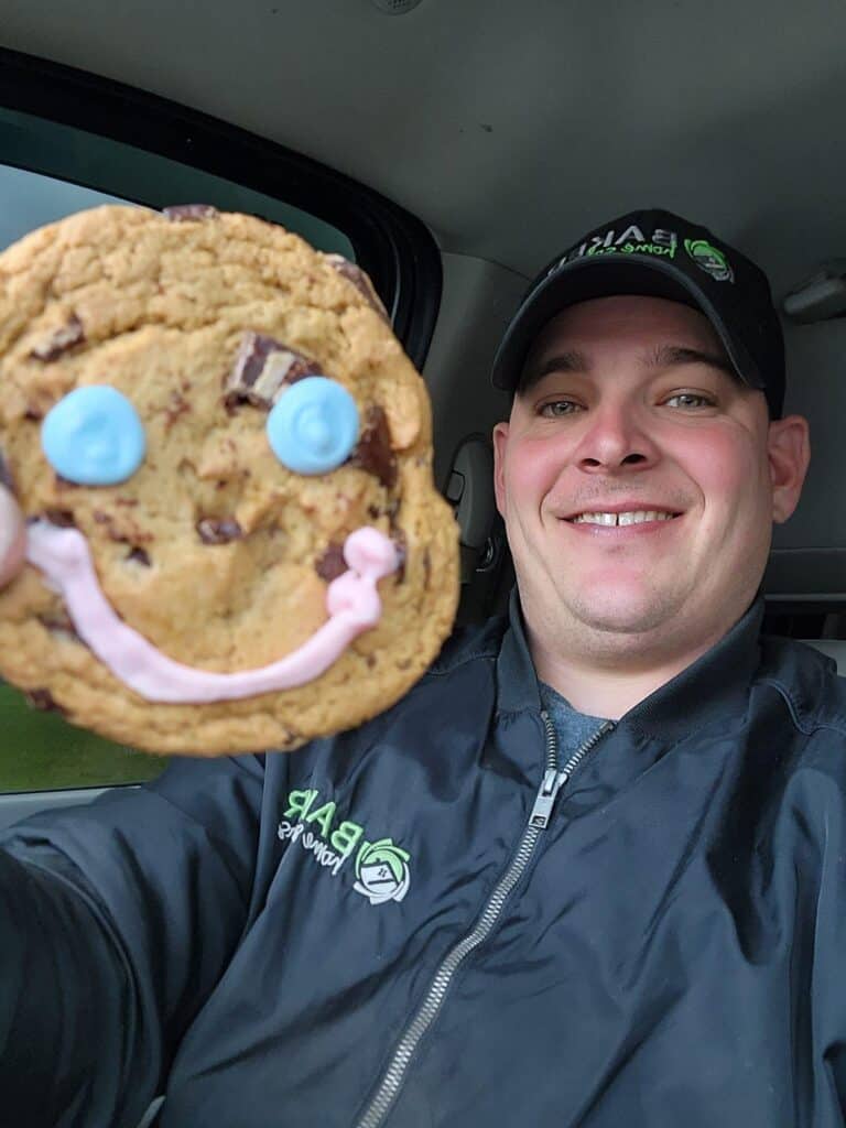 Happy man holding a large smiling cookie in a car, bakery treats, cheerful mood.