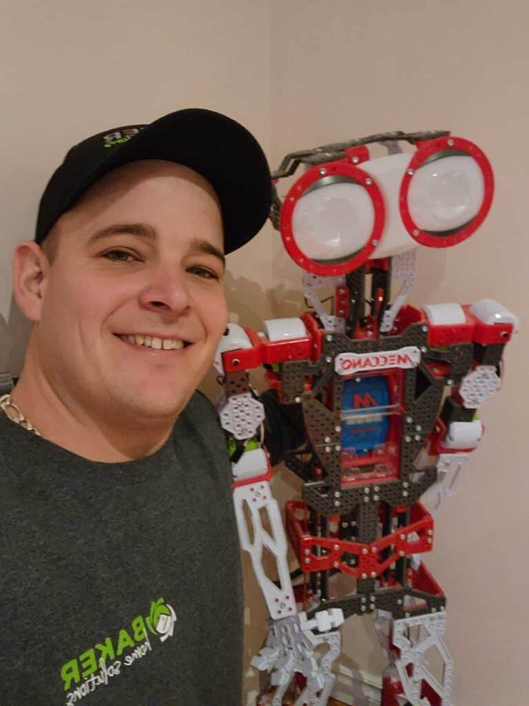 An agile person smiling next to a robot constructed from building blocks.