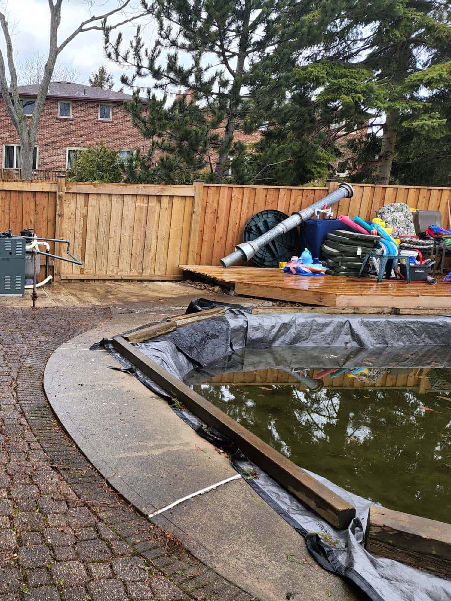 Backyard pond installation site with construction tools, pond liner, and surrounding deck area.